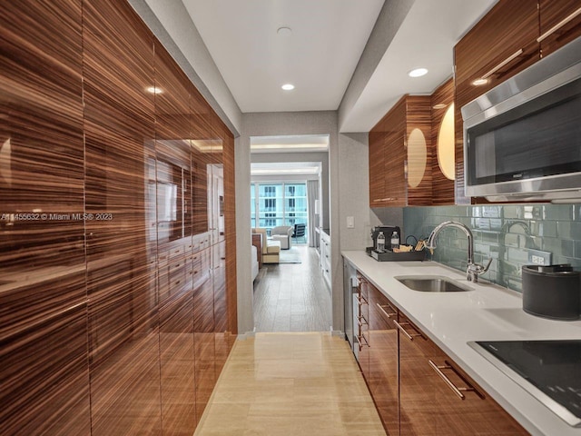 kitchen with black electric stovetop, tasteful backsplash, light wood-type flooring, and sink