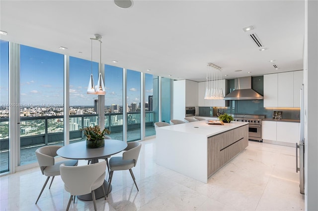 kitchen featuring wall chimney range hood, a wall of windows, white cabinetry, and decorative light fixtures