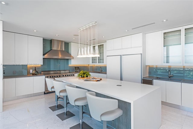 kitchen featuring a kitchen island, wall chimney exhaust hood, decorative light fixtures, built in refrigerator, and decorative backsplash