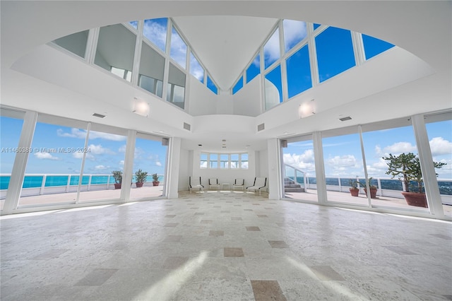 unfurnished living room featuring a high ceiling and a water view