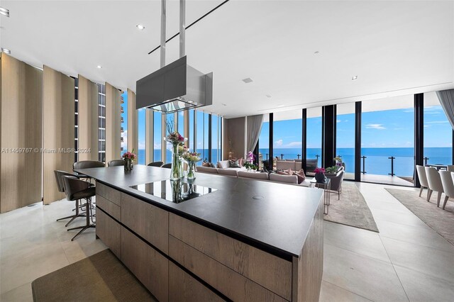 kitchen with light tile floors, plenty of natural light, a kitchen island, expansive windows, and a water view