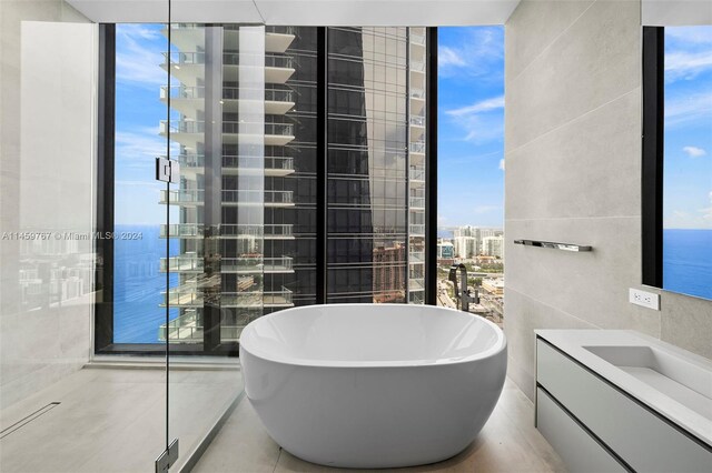 bathroom with vanity, a water view, a bath to relax in, and tile walls