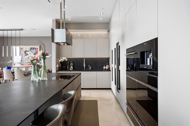 kitchen with light tile floors, wall chimney range hood, white cabinetry, backsplash, and hanging light fixtures