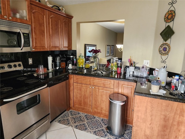 kitchen with appliances with stainless steel finishes, dark stone counters, tasteful backsplash, sink, and light tile patterned floors