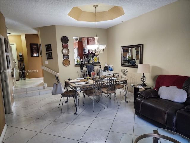 dining area with a notable chandelier, tile patterned floors, a textured ceiling, and a tray ceiling