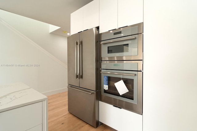 kitchen featuring light stone countertops, light hardwood / wood-style flooring, appliances with stainless steel finishes, and white cabinetry