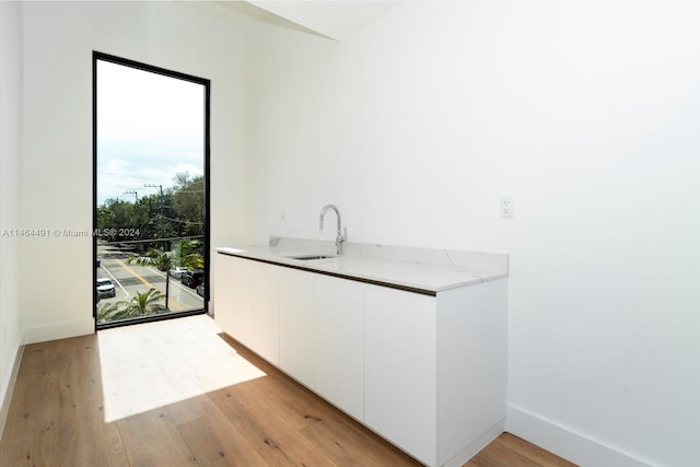 interior space with white cabinets, light stone counters, light hardwood / wood-style floors, and sink