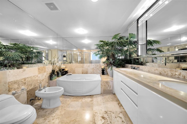 bathroom featuring tile walls, toilet, a bidet, dual vanity, and tile flooring