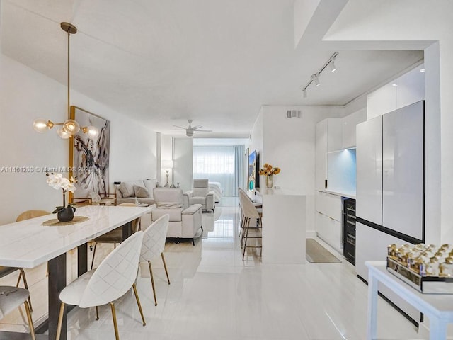 tiled dining space featuring rail lighting and ceiling fan with notable chandelier