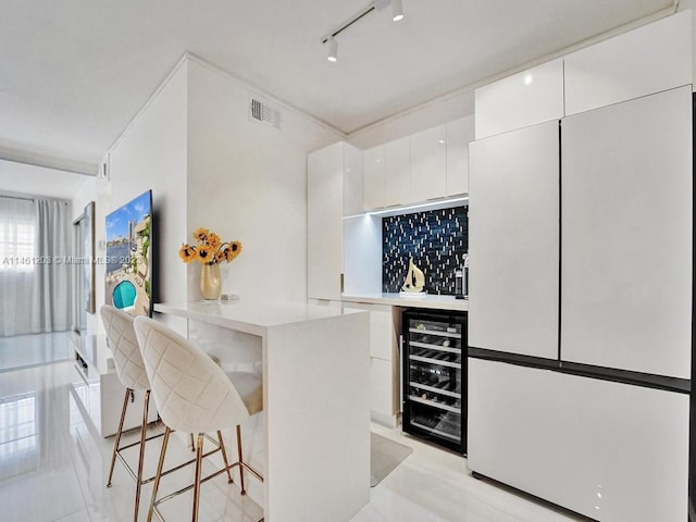 kitchen featuring white cabinetry, beverage cooler, rail lighting, a breakfast bar area, and white refrigerator