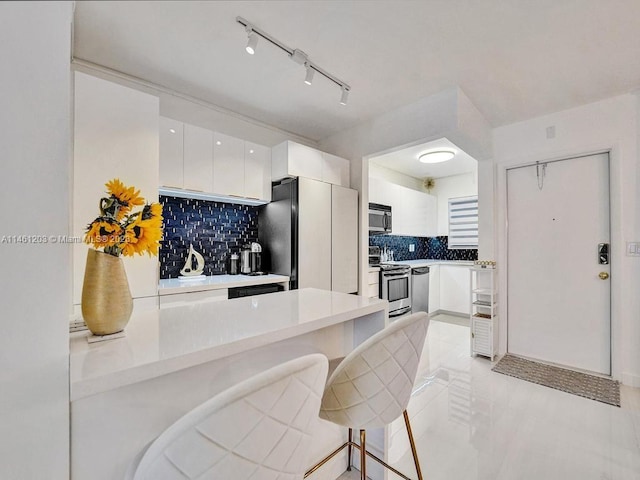 kitchen featuring white cabinets, appliances with stainless steel finishes, a kitchen breakfast bar, and backsplash