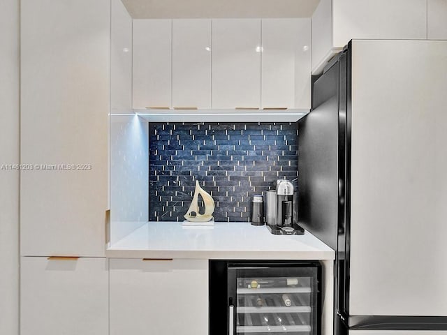 kitchen featuring wine cooler, white cabinets, tasteful backsplash, and black refrigerator