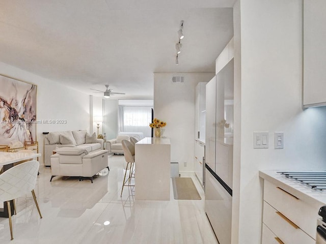 kitchen with light tile floors, ceiling fan, white cabinets, stainless steel refrigerator, and track lighting