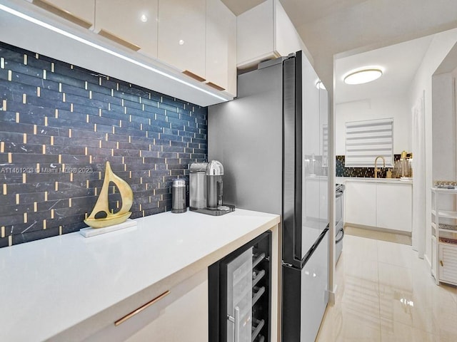 kitchen with light tile flooring, tasteful backsplash, wine cooler, white cabinets, and sink