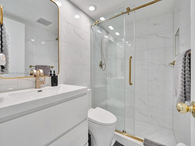 bathroom with tile walls, toilet, a shower with shower door, and large vanity