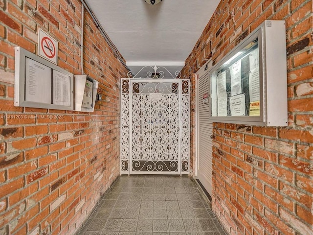 corridor featuring dark tile flooring and brick wall