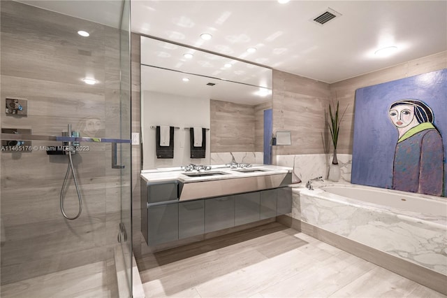 bathroom featuring tile walls, shower with separate bathtub, vanity with extensive cabinet space, tile floors, and dual sinks