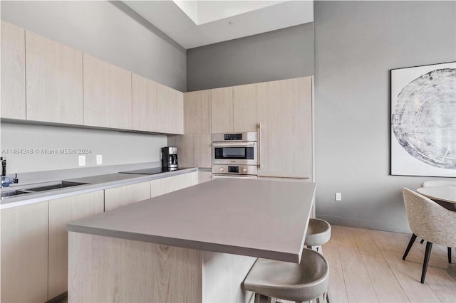 kitchen with stainless steel double oven, a kitchen bar, light brown cabinets, and light hardwood / wood-style floors