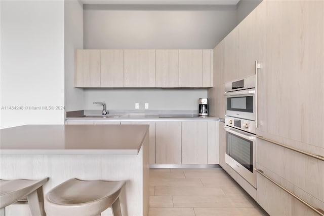 kitchen with kitchen peninsula, cooktop, double oven, sink, and a breakfast bar area