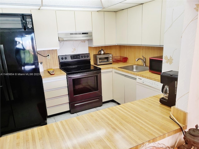 kitchen with light tile flooring, a paneled ceiling, white cabinetry, black appliances, and sink