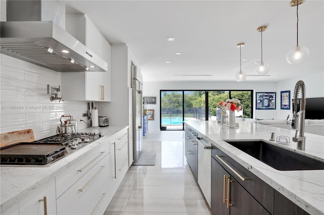 kitchen with white cabinetry, light stone countertops, wall chimney range hood, and sink