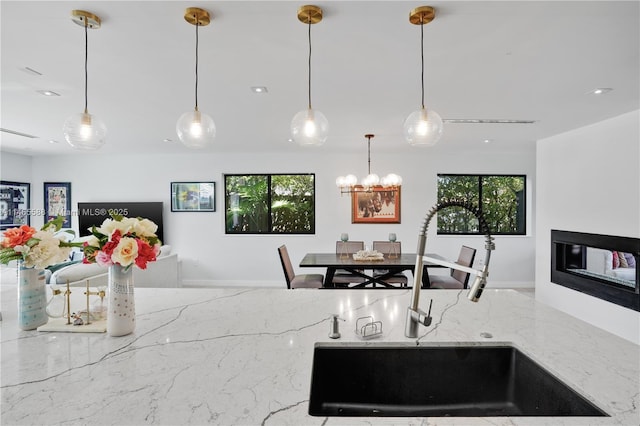 kitchen featuring pendant lighting, light stone counters, a healthy amount of sunlight, and sink