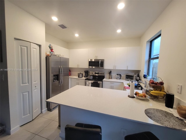 kitchen with appliances with stainless steel finishes, white cabinets, kitchen peninsula, light tile patterned floors, and sink