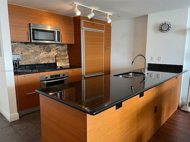 kitchen featuring sink, dark tile flooring, rail lighting, backsplash, and stainless steel appliances