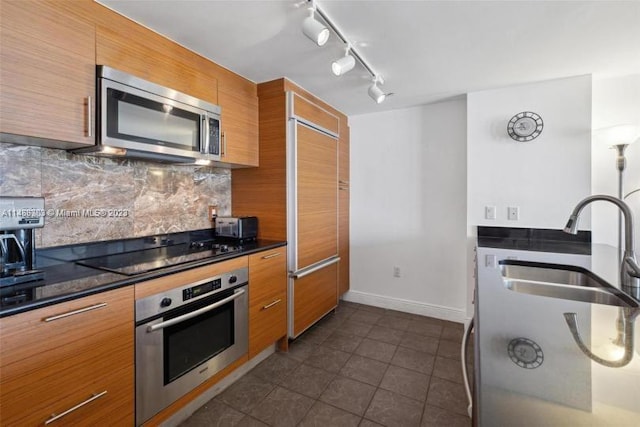 kitchen with dark tile floors, sink, rail lighting, stainless steel appliances, and tasteful backsplash