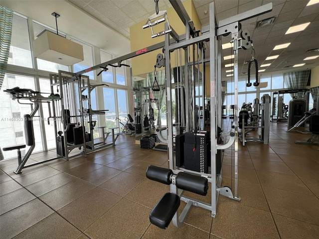 exercise room featuring expansive windows, a towering ceiling, and a drop ceiling