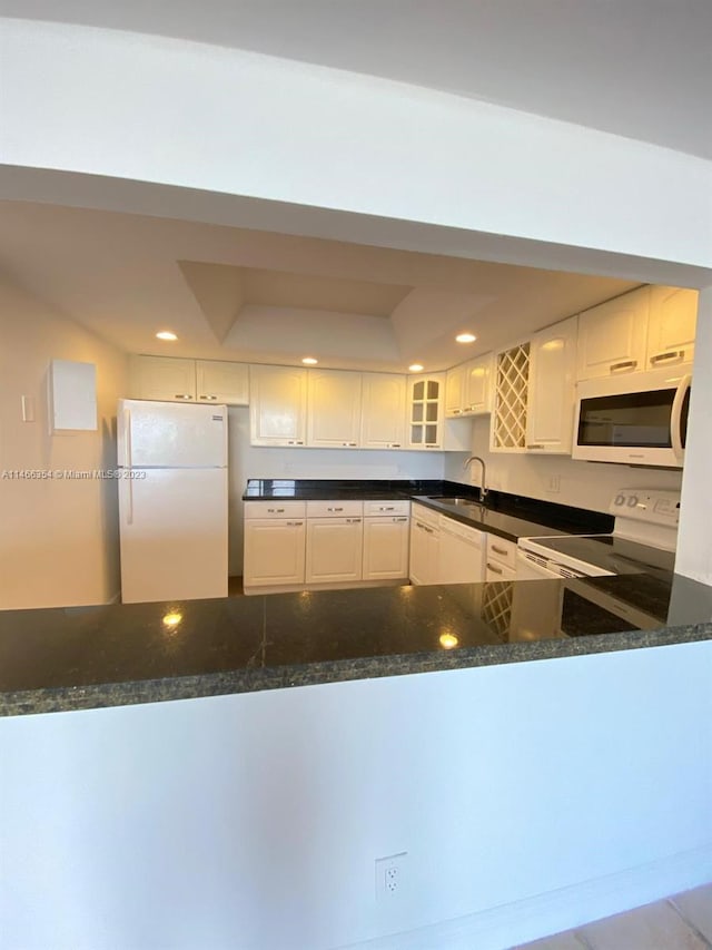 kitchen with dark stone countertops, white appliances, white cabinetry, and sink