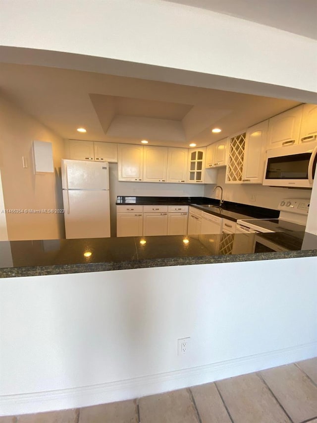 kitchen featuring white appliances, white cabinets, dark stone countertops, and sink