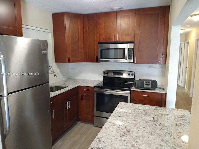 kitchen with light stone countertops, tasteful backsplash, appliances with stainless steel finishes, light wood-type flooring, and sink