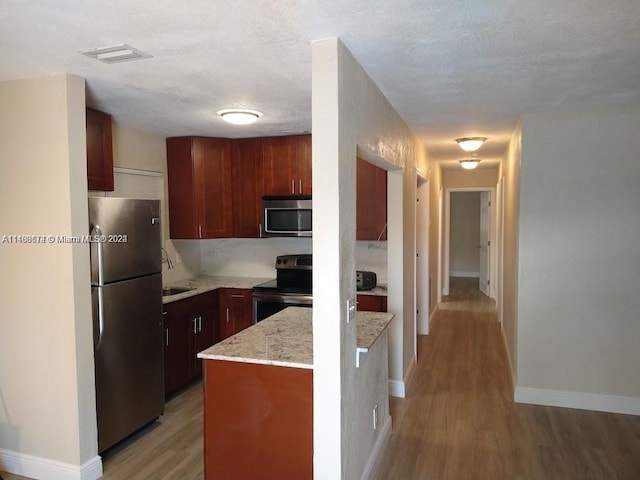 kitchen featuring light hardwood / wood-style floors, a textured ceiling, appliances with stainless steel finishes, light stone counters, and sink