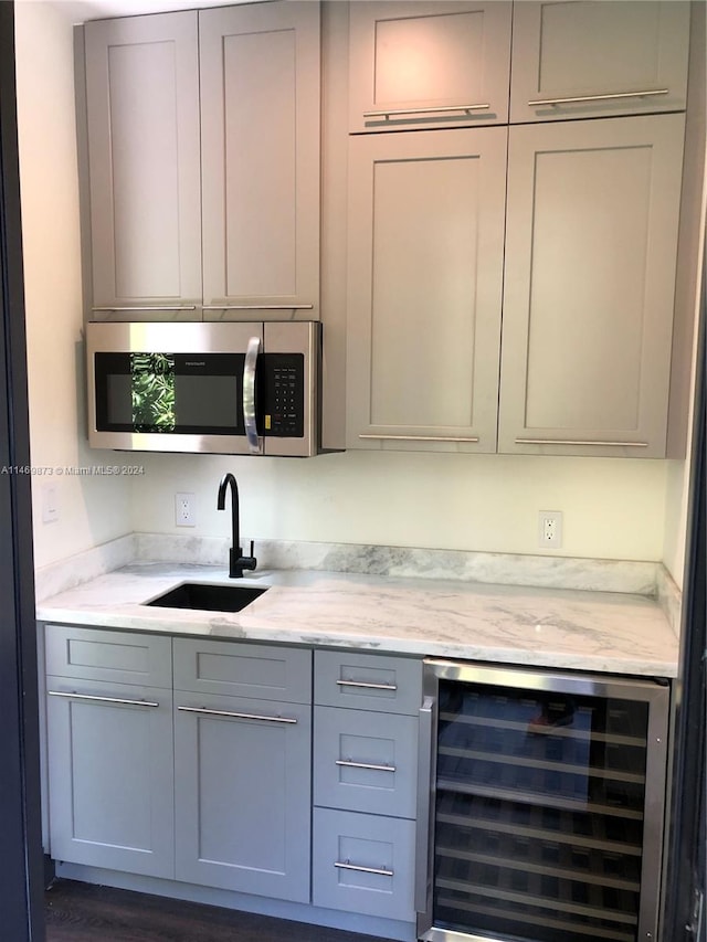 bar with light stone counters, sink, gray cabinetry, and beverage cooler