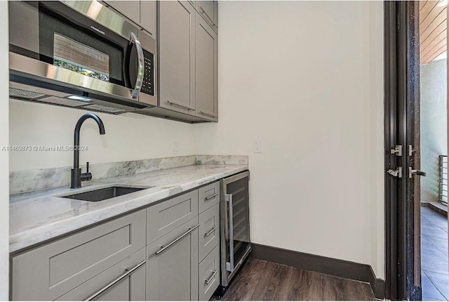 kitchen with gray cabinetry, sink, light stone counters, and beverage cooler