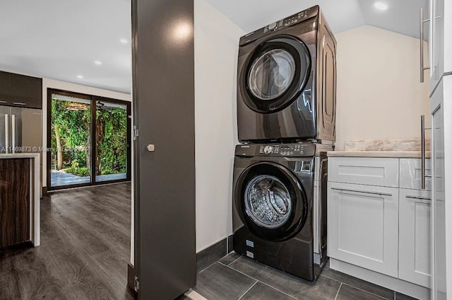 clothes washing area with stacked washer / dryer, dark hardwood / wood-style floors, and cabinets