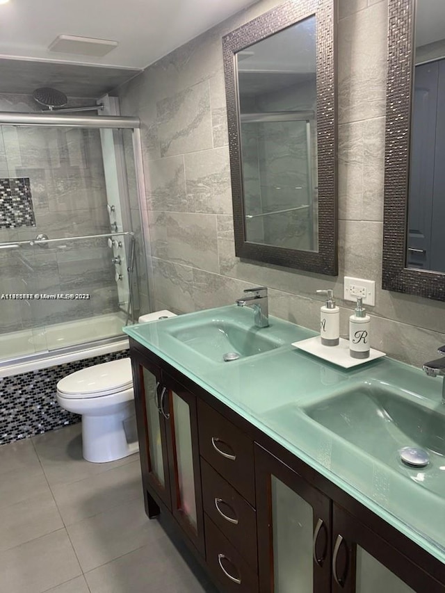 full bathroom with double sink, vanity with extensive cabinet space, toilet, and tile walls