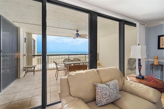 tiled living room with ceiling fan, a wall of windows, crown molding, a view of the beach, and a water view