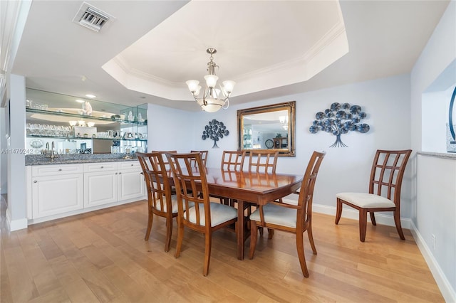 dining area featuring ornamental molding, a tray ceiling, light hardwood / wood-style floors, and a notable chandelier