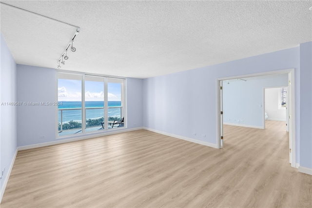 unfurnished room with a textured ceiling, rail lighting, and light hardwood / wood-style floors