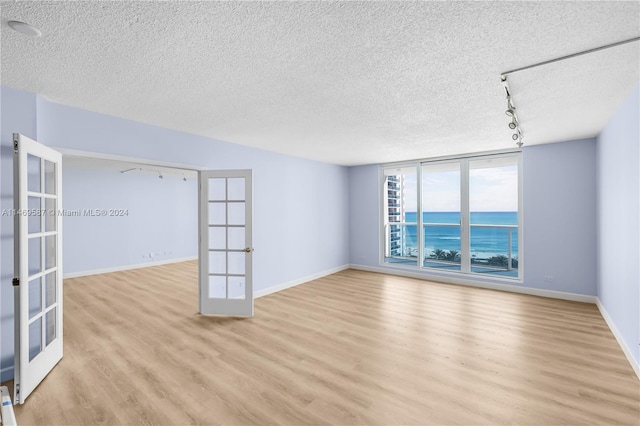 empty room featuring french doors, light hardwood / wood-style floors, and a textured ceiling