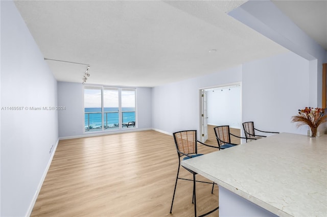 dining area featuring a water view, a textured ceiling, light wood-type flooring, and track lighting