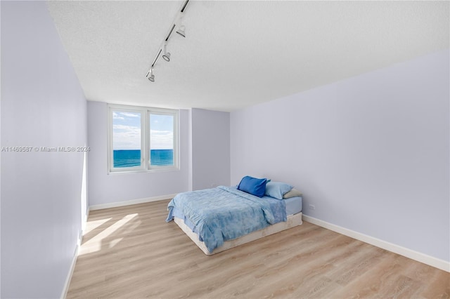 bedroom with light hardwood / wood-style floors, a textured ceiling, and track lighting