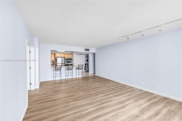 unfurnished living room featuring light hardwood / wood-style floors, a textured ceiling, and track lighting