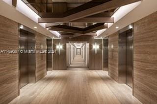 hallway featuring light hardwood / wood-style floors, wooden walls, and beamed ceiling