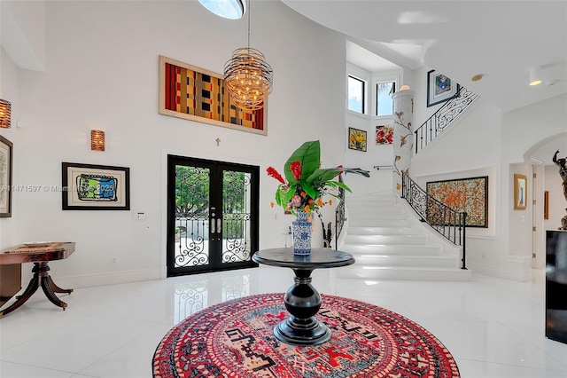 tiled foyer entrance with arched walkways, a towering ceiling, baseboards, french doors, and stairway