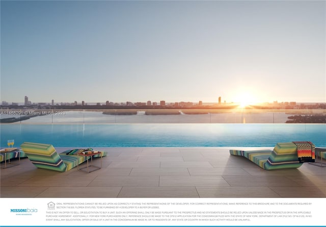 pool at dusk featuring a water view and a patio