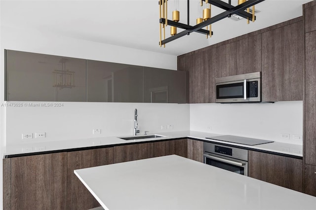 kitchen with an inviting chandelier, appliances with stainless steel finishes, sink, dark brown cabinetry, and pendant lighting