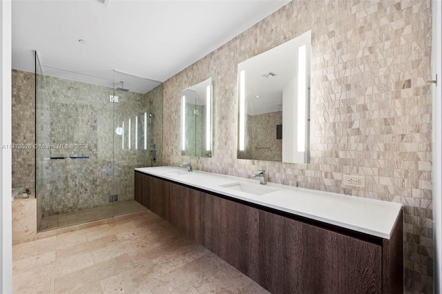 bathroom with a shower with door, dual bowl vanity, tile flooring, and tile walls